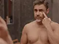 Mężczyzna z siwiejącą brodą ogląda w lustrze swoje zmarszczki pod oczami, zastanawiając się nad pielęgnacją.