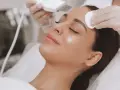 Kobieta po 30. przechodzi zabieg oczyszczania twarzy. Kosmetolog wykonuje peeling kawitacyjny, poprawiając kondycję skóry.