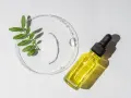 Kropla białego kremu i żółte serum w buteleczce z pipetką, obok gałązka z liśćmi. Składniki do walki z trądzikiem, w tym retinol.