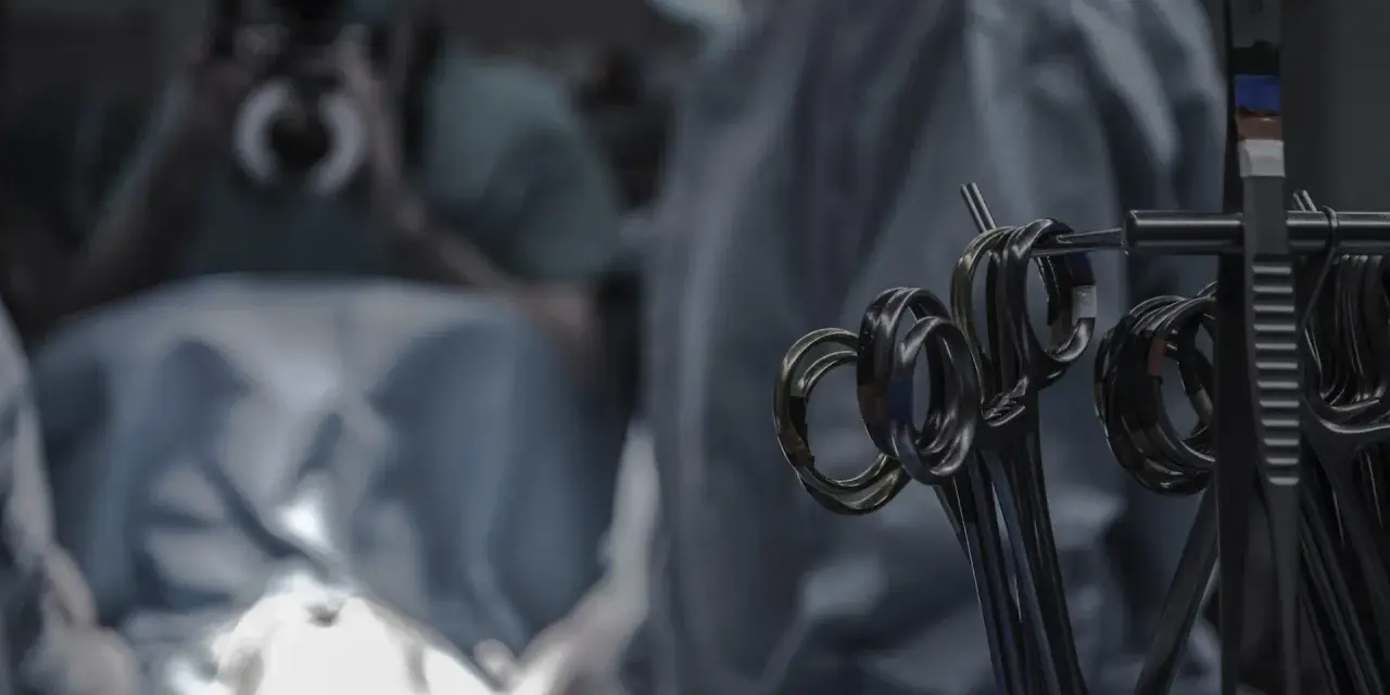 Narzędzia chirurgiczne w zbliżeniu. W tle niewyraźny zespół medyczny podczas procedury, która może być operacją lub zabiegiem.