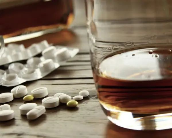 Tabletki i szklanka z alkoholem. Zastanawiasz się, po jakim czasie od zastrzyku można pić alkohol? To ważne pytanie.