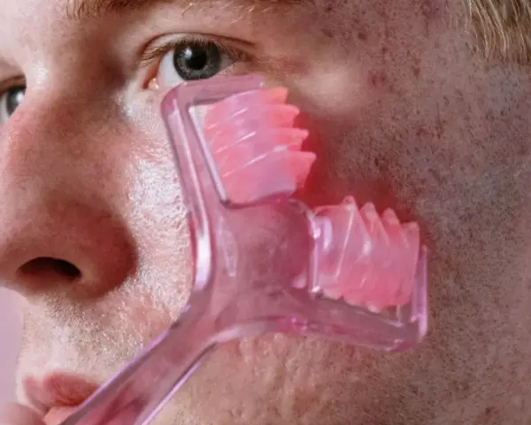Mężczyzna z trądzikiem na twarzy używa różowego masażera do skóry.
